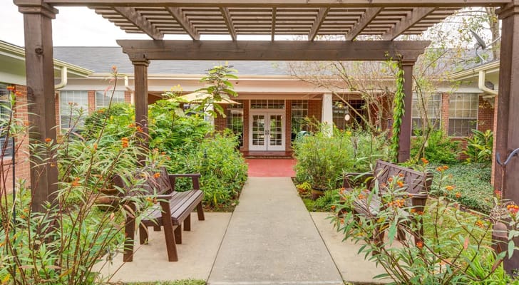 A garden pathway lined with benches leading to the entrance of The Auberge at Sugar Land.