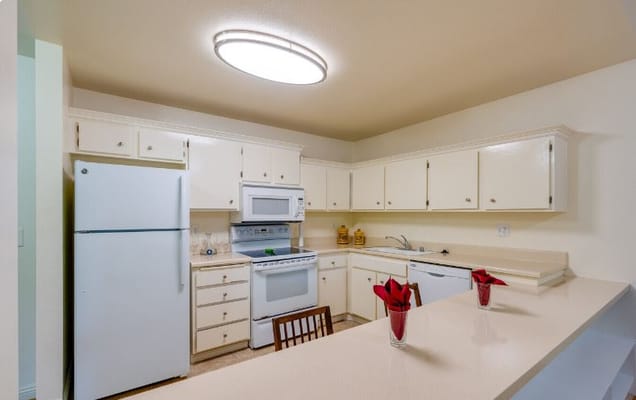 View of a well-equipped kitchen with white cabinets, appliances, and decorative flowers.