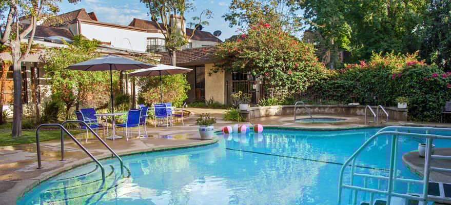 Outdoor pool with lounge chairs and umbrellas at The Oaks of Pasadena