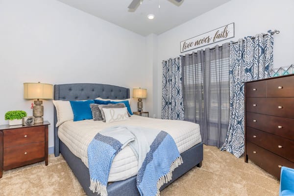 A beautifully decorated senior living bedroom with a bed, nightstand, and curtains.