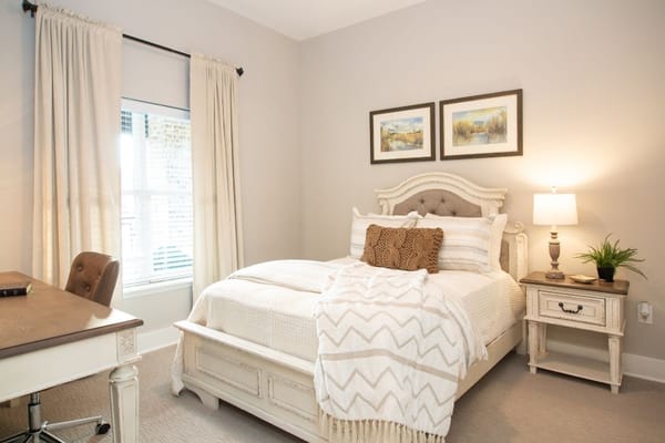 Brightly lit bedroom with a bed, desk, and decorative furnishings.