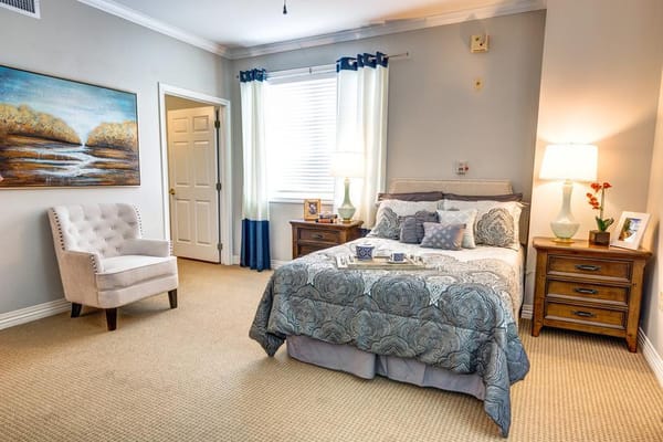 A well-decorated private resident room with a bed and chair