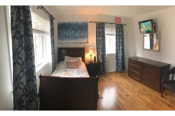 A comfortable bedroom featuring a single bed, dresser, and a television.