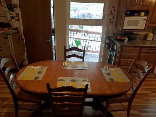 A wooden dining table set with placemats and glasses, overlooking a sunny patio.