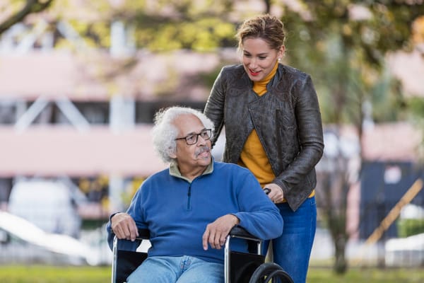 Elderly man in a wheelchair outdoors with staff member