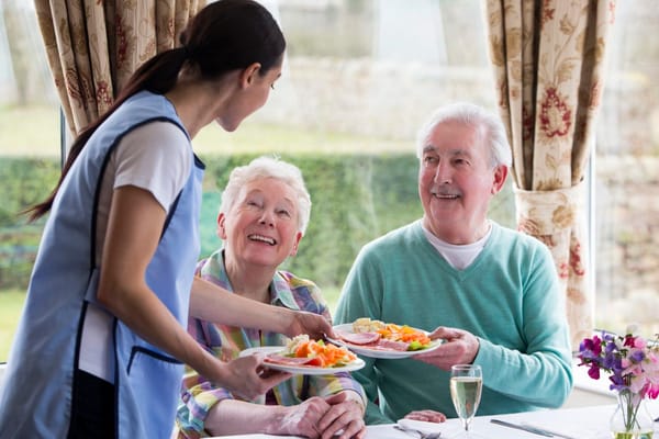 Staff serving food to smiling residents in a dining room