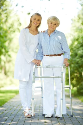 A caregiver assisting a resident outdoors with a walker