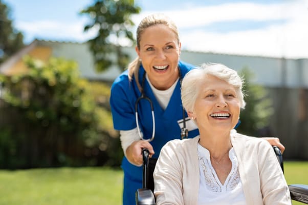 Caregiver assisting a smiling resident outdoors.