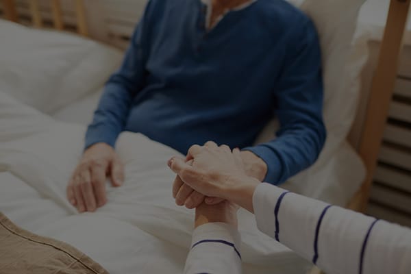Hands clasped by a patient and caregiver in bed
