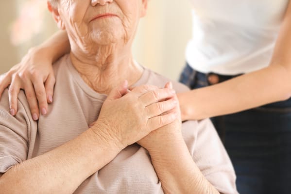 A close-up of a caregiver's hand on a senior's shoulder