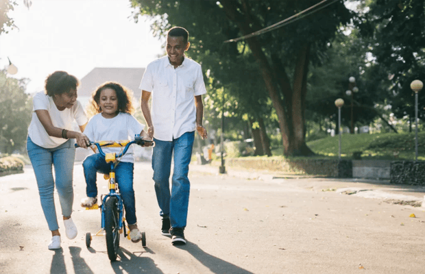 Family assisting a child riding a bicycle in a park