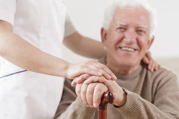 An elderly man smiling with a caregiver's hands on top of his