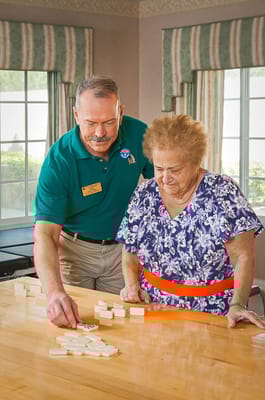Staff assisting a resident with a game of dominoes