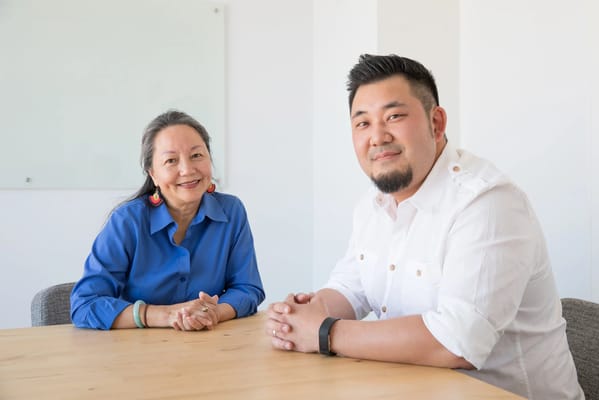 A woman and a man smiling at a table in a bright room