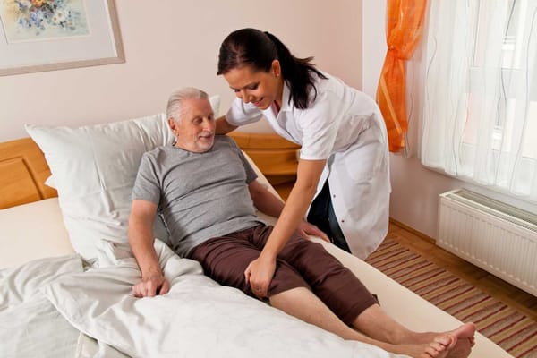 A caregiver assisting a senior man in a bedroom
