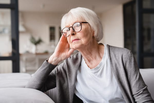 An older woman sitting thoughtfully in a bright interior