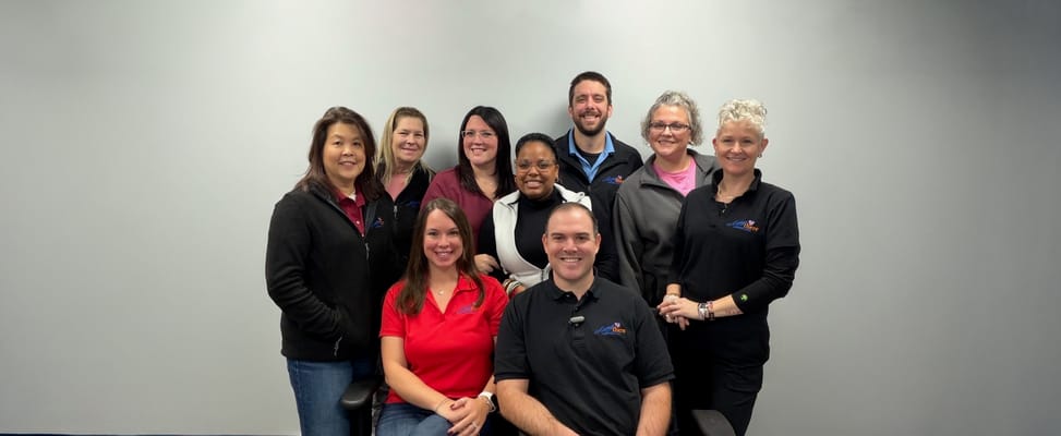Team of staff members posing together in front of a gray background