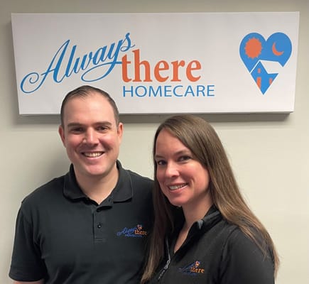 Two staff members posing in front of the facility sign