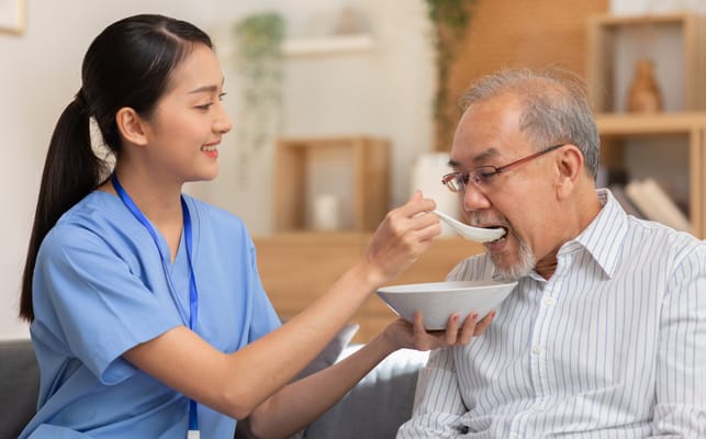 A caregiver feeding a resident in a cozy living space