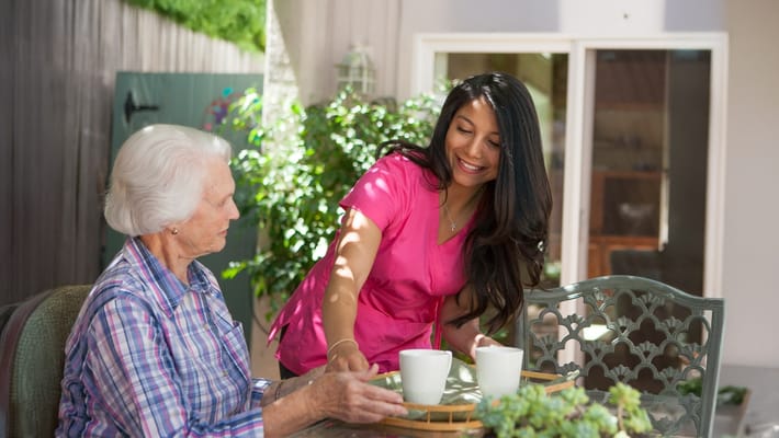 Caregiver serving tea to a senior resident outdoors