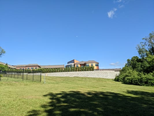 A building at Carleton-Willard Village surrounded by green grass and a fence under a clear blue sky.