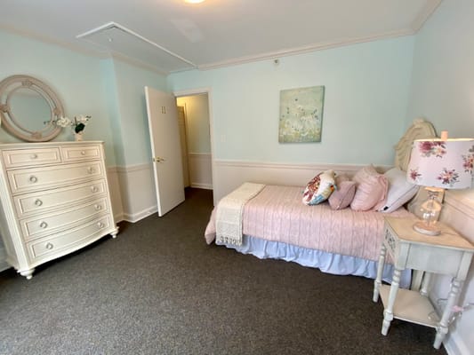 A well-furnished bedroom featuring a bed, dresser, and soft decor.