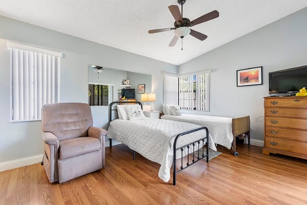 Cozy bedroom with two beds, a recliner, and a dresser in Westbridge Assisted Living Facility