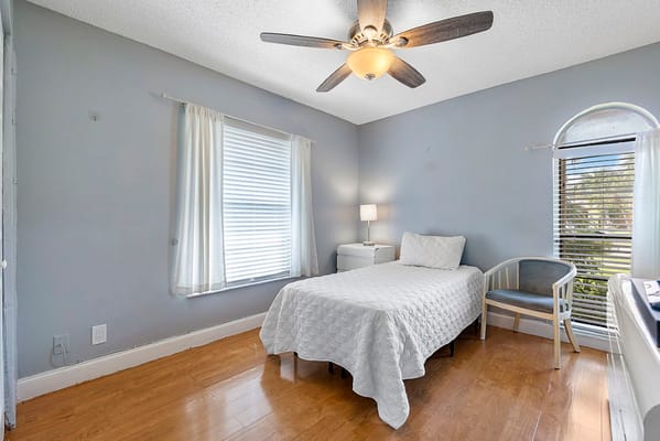 Bedroom with a single bed, lamp, and window in Westbridge Assisted Living Facility