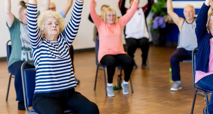 Seniors participating in a seated exercise class indoors
