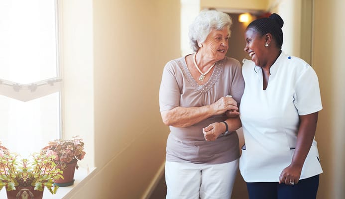 A resident and caregiver smiling in a hallway