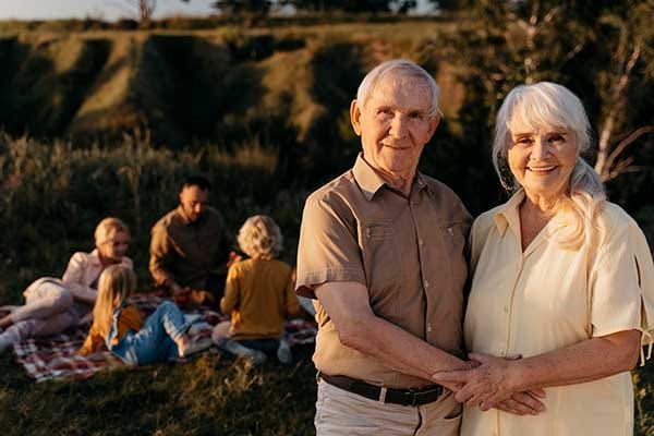Elderly couple enjoying a picnic outdoors with family in background