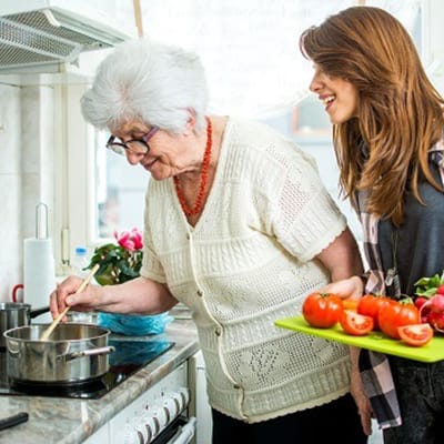 A caregiver assisting an elderly woman in the kitchen