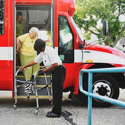 Senior resident assisted by staff exiting a facility van