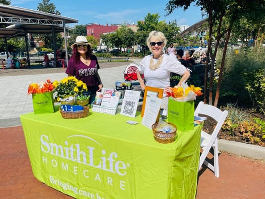 Two women at a table promoting SmithLife Homecare with flowers and informational materials.