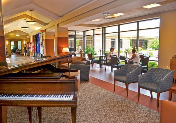 Common area with piano and seating, sunlight coming through windows
