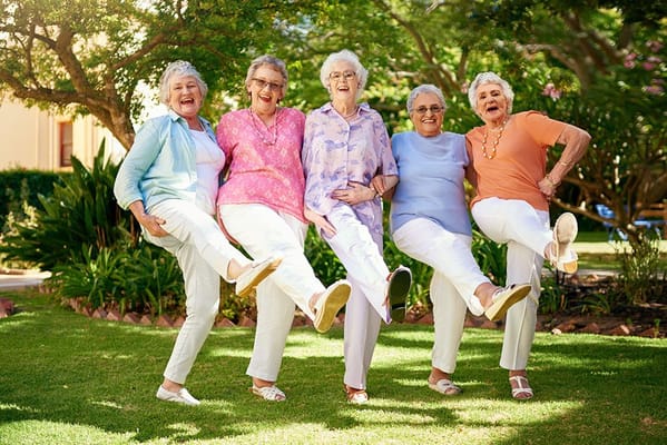 Five joyful senior women lifting their legs in a garden