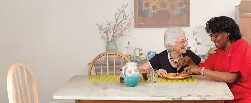 Staff assisting a resident with a meal at a table