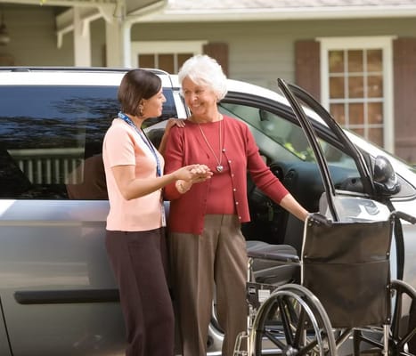 Caregiver assisting elderly woman near a vehicle