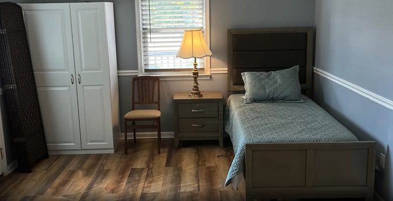 A small, cozy bedroom with a bed, lamp, and chair.