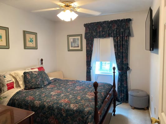 A cozy bedroom with a floral bedspread, a small couch, curtains, and a TV.