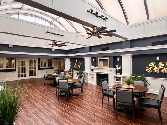 Spacious common area with tables and plants in Brookhaven Health Care Facility.