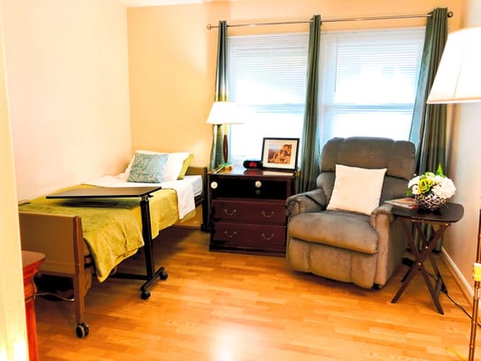 A cozy bedroom featuring a hospital bed, a recliner, and a bedside table with lamps.