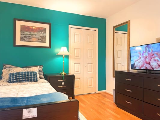 A well-decorated bedroom featuring a bed, lamp, dresser, and TV.