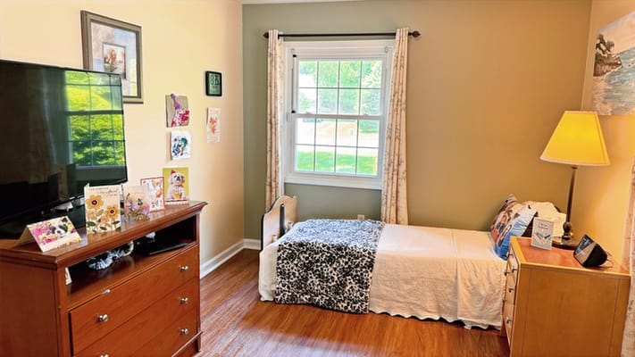 A cozy bedroom featuring a bed, dresser, and a large window.