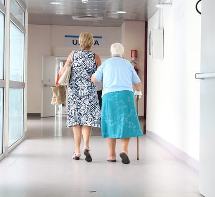Two women walking down a corridor, one with a cane