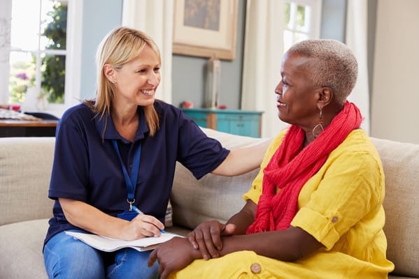 A caregiver and a senior woman smiling and talking in a cozy living room.