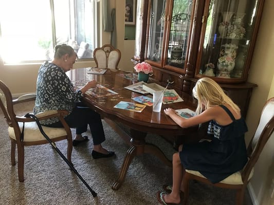 An older woman working on a puzzle with a young girl at a wooden table.