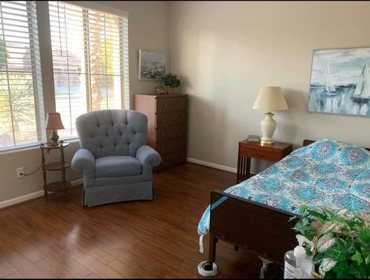 A cozy bedroom with a bed, a blue chair, and a dresser.
