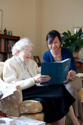 A staff member reading with a senior resident in a cozy interior.