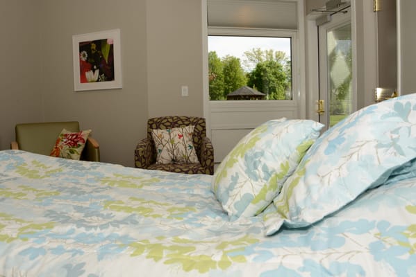 A well-decorated bedroom with a floral bedspread, a chair, and a view of nature outside.